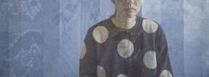 A person's torso in a spotty jumper behind a curtain, with only the lower part of their face visible