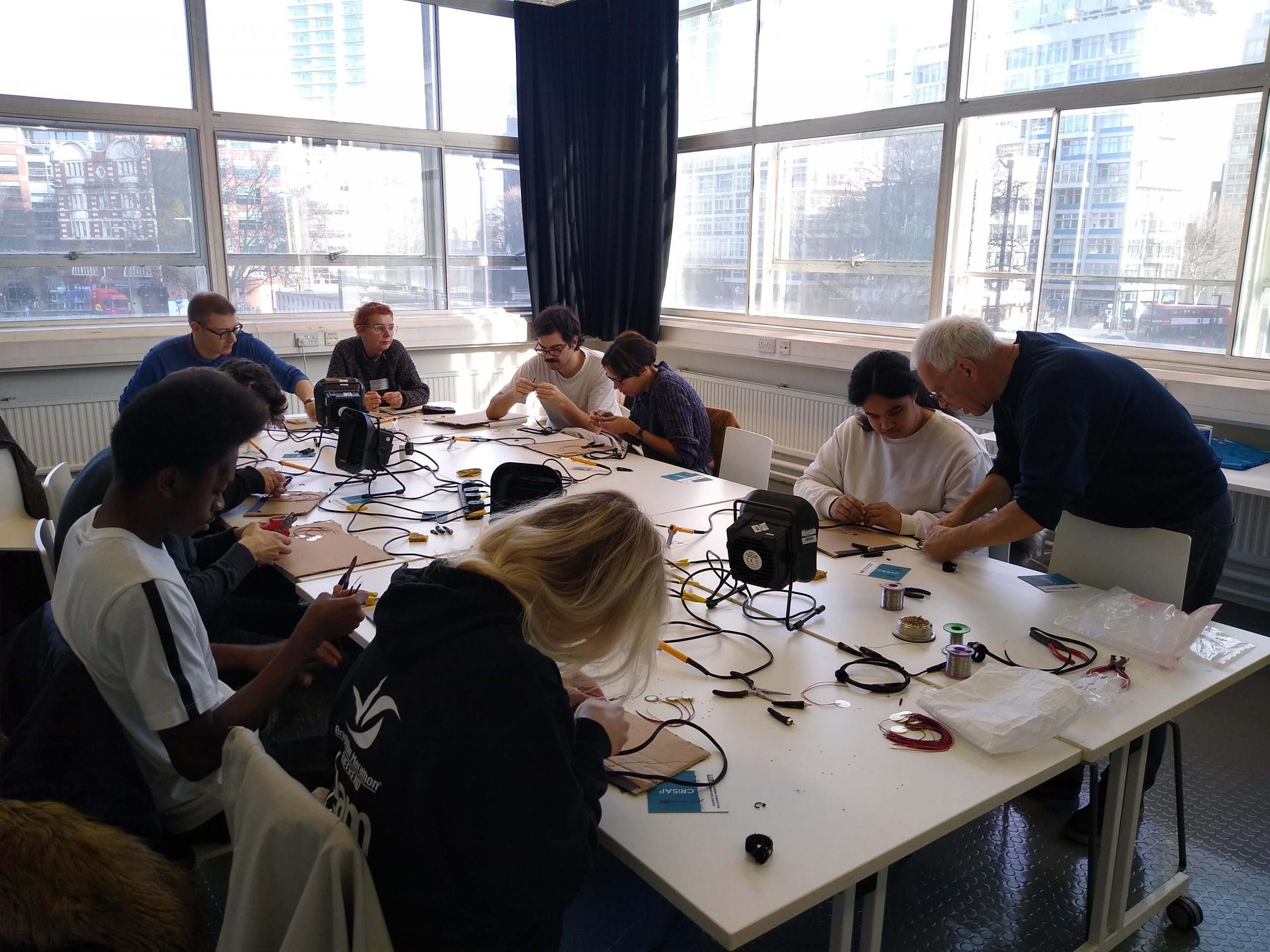 A room with 8 people working at a table covered in wires