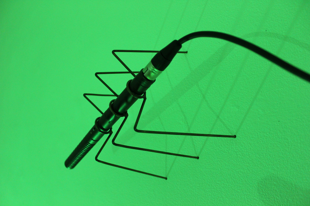 A long thin microphone with wire 'legs' against a green background
