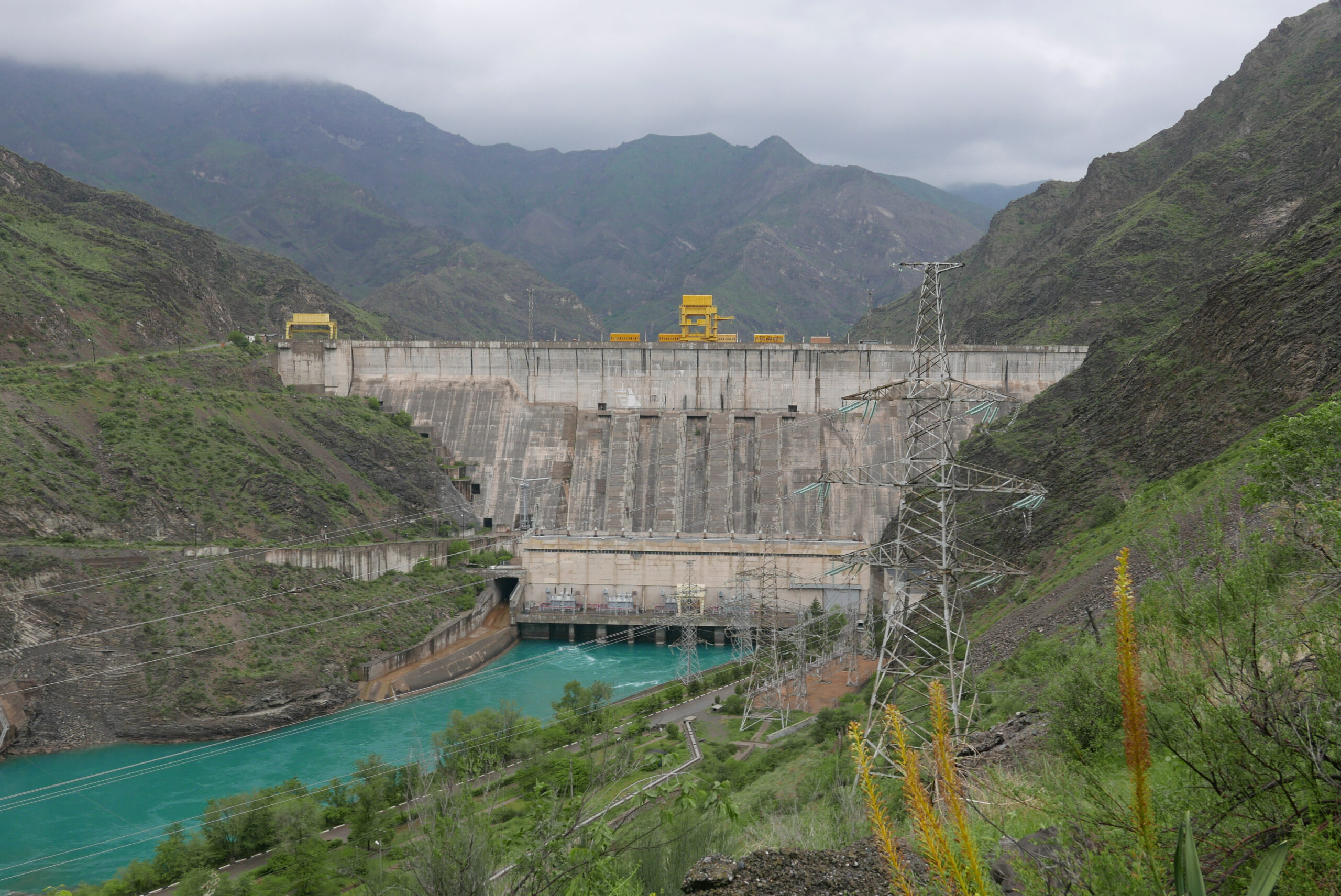 The Kurpsai hydroelectric dam in Kyrgyzstan - a large concorete damn set in mountains with a bright green river running from the bottom of the damn