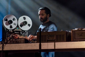 Paul Pergas stands on a stage turning dials on a sound mixing desk