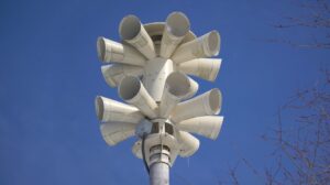 Several tube-like speakers protrude from a tall pole with blue skies in the background